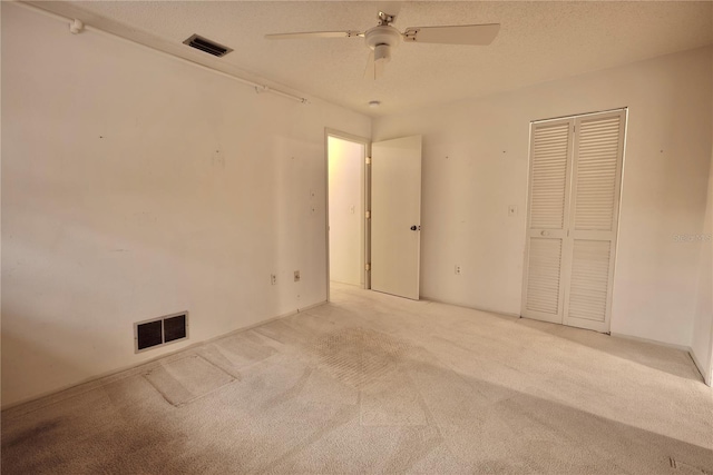 unfurnished bedroom featuring ceiling fan, a closet, light carpet, and a textured ceiling