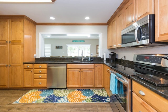 kitchen with sink, crown molding, light hardwood / wood-style flooring, appliances with stainless steel finishes, and dark stone countertops