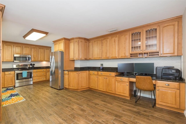 kitchen featuring stainless steel appliances, dark hardwood / wood-style floors, built in desk, and dark stone counters