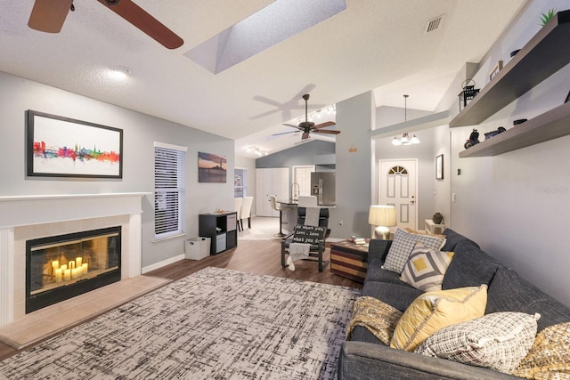 living room with a tile fireplace, vaulted ceiling, dark wood-type flooring, sink, and ceiling fan with notable chandelier