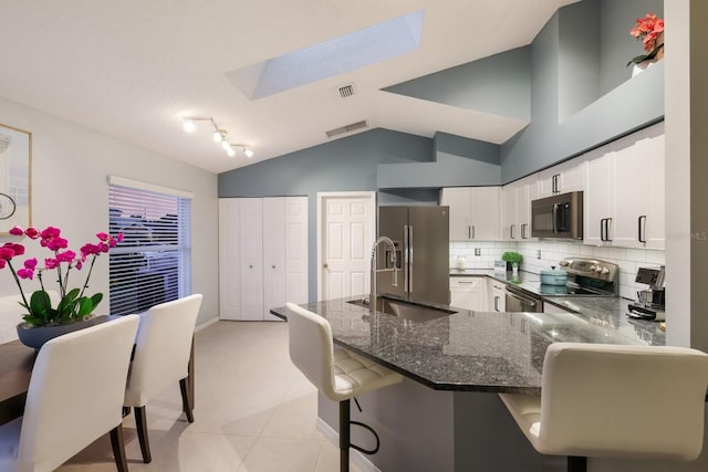 kitchen featuring stainless steel appliances, white cabinetry, kitchen peninsula, a breakfast bar area, and lofted ceiling with skylight