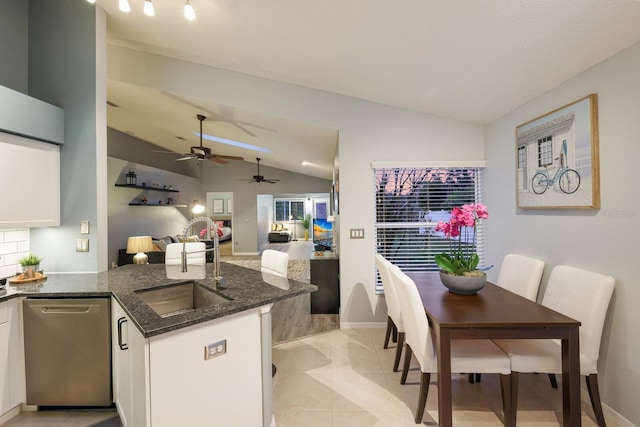 kitchen with kitchen peninsula, dark stone counters, white cabinetry, stainless steel dishwasher, and lofted ceiling