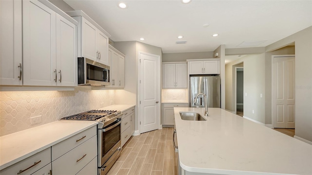 kitchen featuring stainless steel appliances, a kitchen island with sink, white cabinets, and sink