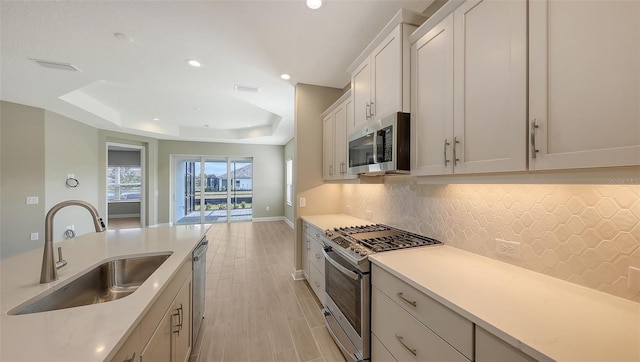 kitchen featuring sink, white cabinetry, a raised ceiling, backsplash, and appliances with stainless steel finishes