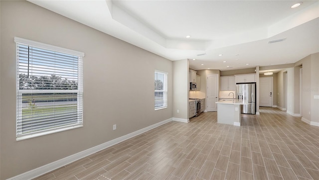 unfurnished living room with sink, light hardwood / wood-style floors, and a tray ceiling