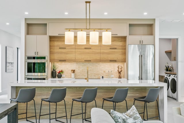 kitchen featuring separate washer and dryer, appliances with stainless steel finishes, a kitchen island, decorative light fixtures, and tasteful backsplash