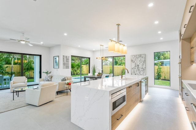 kitchen with light stone countertops, decorative light fixtures, a large island, ceiling fan with notable chandelier, and sink