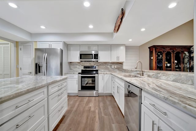 kitchen with light hardwood / wood-style flooring, appliances with stainless steel finishes, white cabinetry, light stone countertops, and decorative backsplash