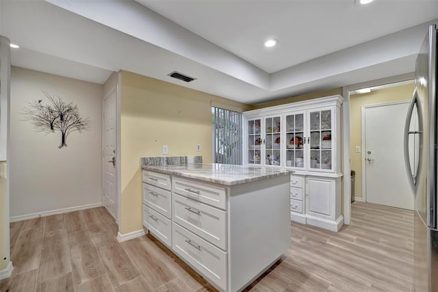 kitchen with white cabinets, light hardwood / wood-style flooring, stainless steel fridge, and light stone counters