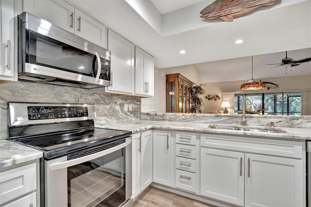 kitchen with light stone countertops, appliances with stainless steel finishes, white cabinetry, decorative backsplash, and sink