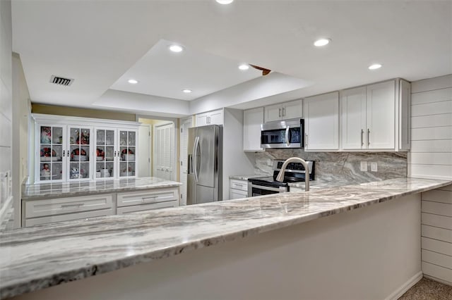 kitchen with white cabinets, a tray ceiling, light stone counters, decorative backsplash, and stainless steel appliances