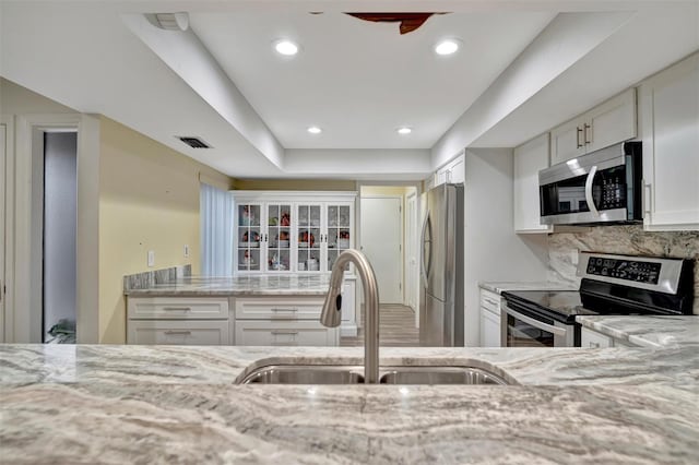 kitchen featuring sink, white cabinets, tasteful backsplash, light stone counters, and stainless steel appliances