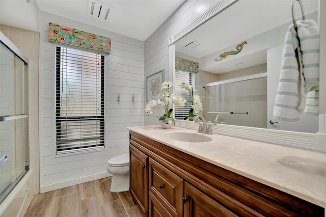 full bathroom with wooden walls, toilet, a wealth of natural light, and vanity