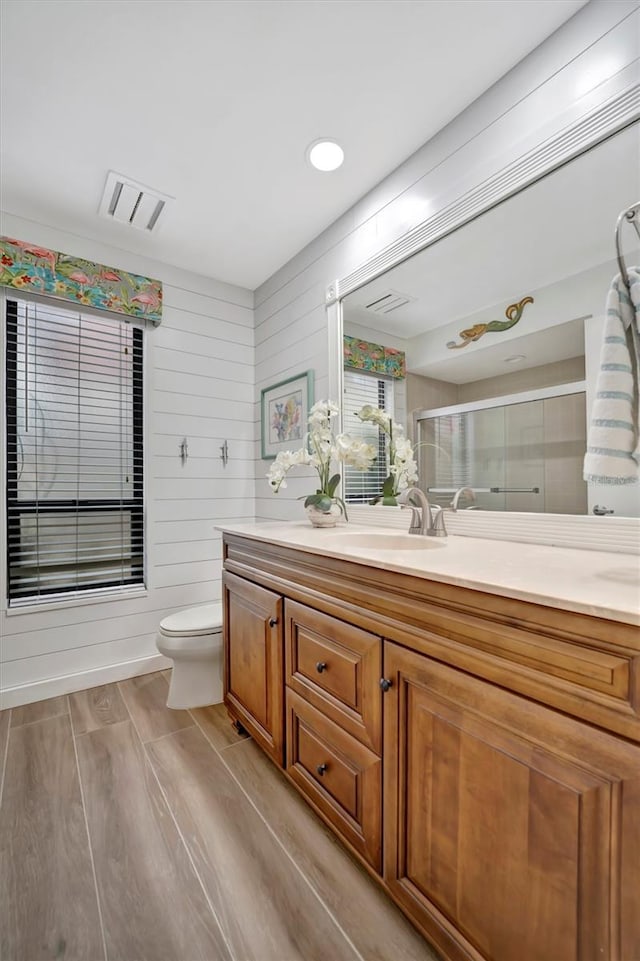 bathroom with a shower with shower door, toilet, vanity, and wood walls