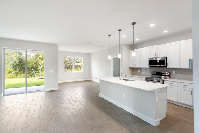 kitchen featuring pendant lighting, sink, appliances with stainless steel finishes, white cabinetry, and a center island with sink