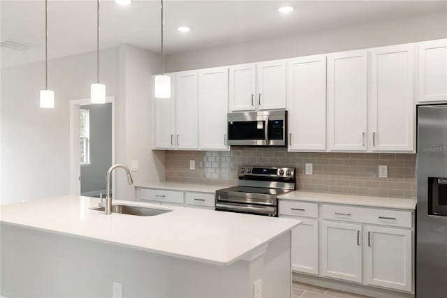 kitchen with sink, appliances with stainless steel finishes, white cabinetry, an island with sink, and decorative light fixtures