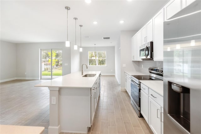 kitchen with sink, a center island with sink, appliances with stainless steel finishes, pendant lighting, and white cabinets