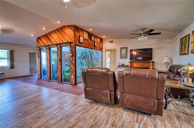 living room with lofted ceiling, a textured ceiling, ceiling fan, and light wood-type flooring