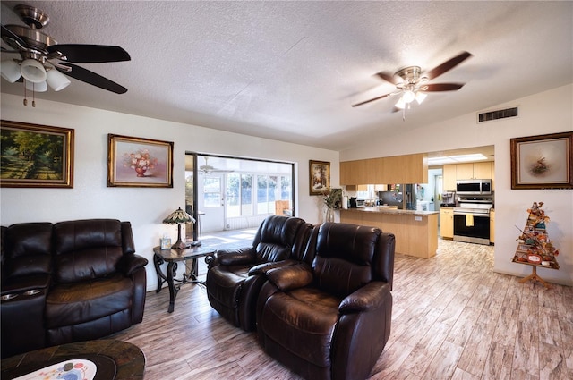 living room with ceiling fan, lofted ceiling, a textured ceiling, and light wood-type flooring