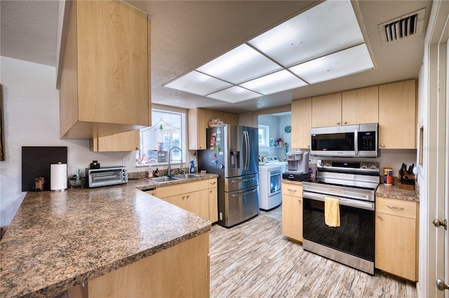 kitchen with sink, light hardwood / wood-style flooring, light brown cabinets, stainless steel appliances, and washer / clothes dryer