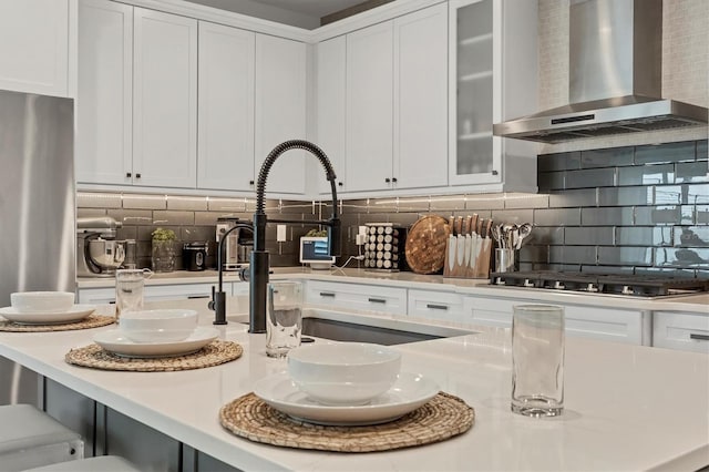 kitchen featuring white cabinets, wall chimney exhaust hood, stainless steel appliances, and tasteful backsplash