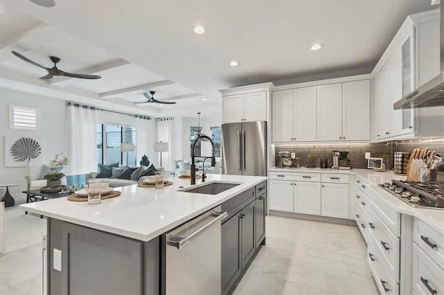 kitchen with wall chimney range hood, white cabinets, stainless steel appliances, and an island with sink