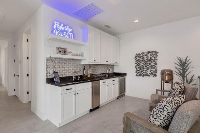 bar with tasteful backsplash, white cabinets, sink, and beverage cooler