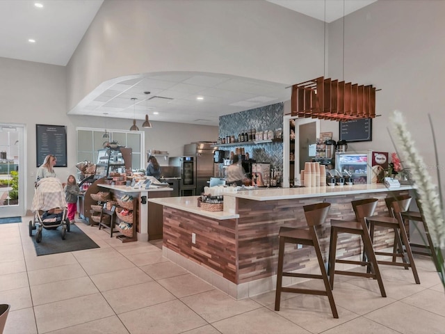 kitchen with light tile patterned floors, kitchen peninsula, a breakfast bar area, a towering ceiling, and stainless steel refrigerator