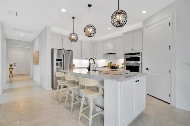 kitchen featuring sink, pendant lighting, stainless steel appliances, a kitchen island with sink, and white cabinets