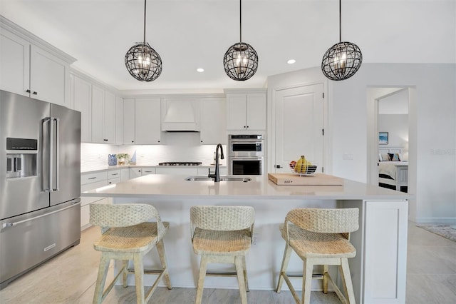 kitchen featuring custom exhaust hood, appliances with stainless steel finishes, white cabinets, sink, and an island with sink