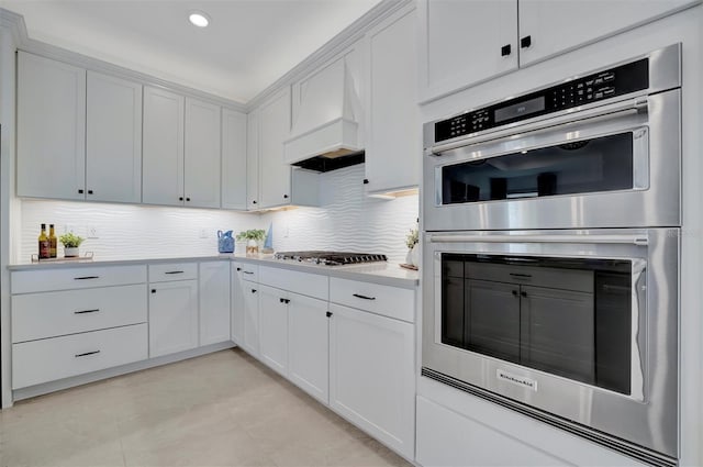 kitchen with premium range hood, backsplash, white cabinetry, and appliances with stainless steel finishes