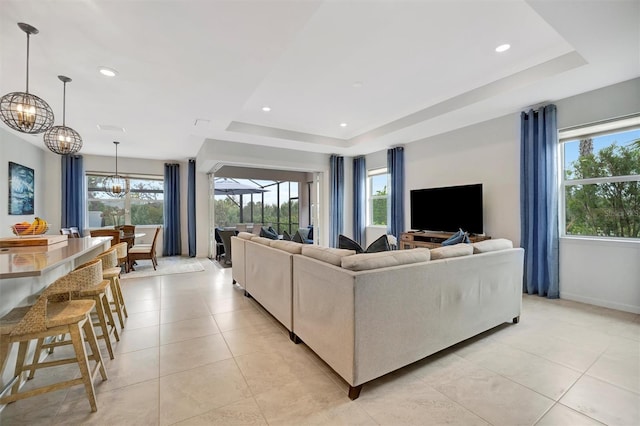 tiled living room featuring a raised ceiling and a chandelier