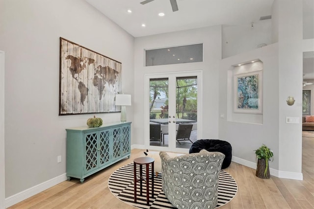 sitting room featuring a towering ceiling, ceiling fan, light hardwood / wood-style flooring, and french doors