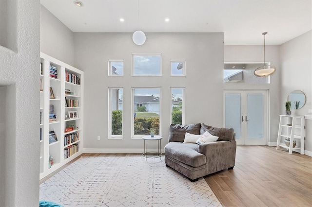 sitting room with a high ceiling, built in features, french doors, and light wood-type flooring