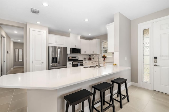 kitchen with sink, white cabinetry, kitchen peninsula, a breakfast bar area, and appliances with stainless steel finishes