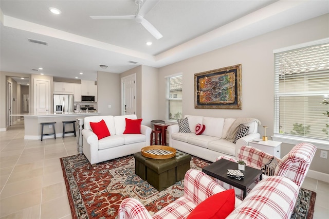 tiled living room featuring ceiling fan and a raised ceiling