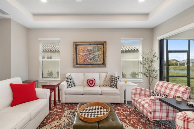 living room featuring a tray ceiling and a water view