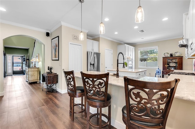 kitchen featuring an island with sink, ornamental molding, stainless steel fridge, white cabinets, and decorative light fixtures