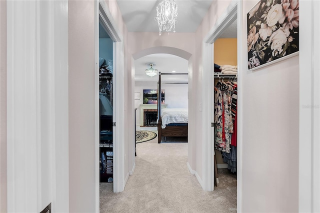 hall featuring carpet flooring, arched walkways, and a chandelier