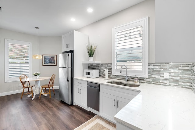 kitchen with pendant lighting, dishwashing machine, stainless steel refrigerator, white cabinets, and sink