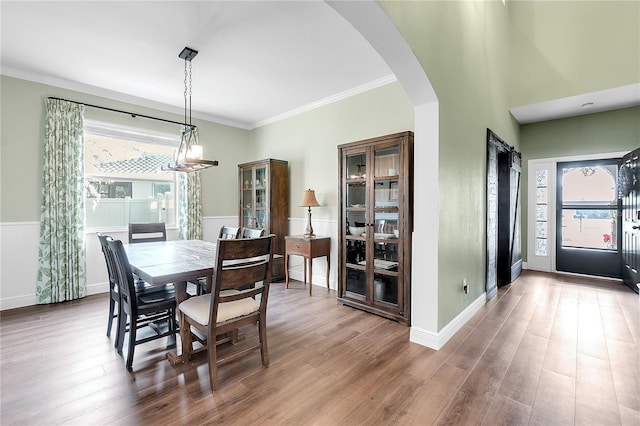 dining space with arched walkways, a wainscoted wall, ornamental molding, and wood finished floors