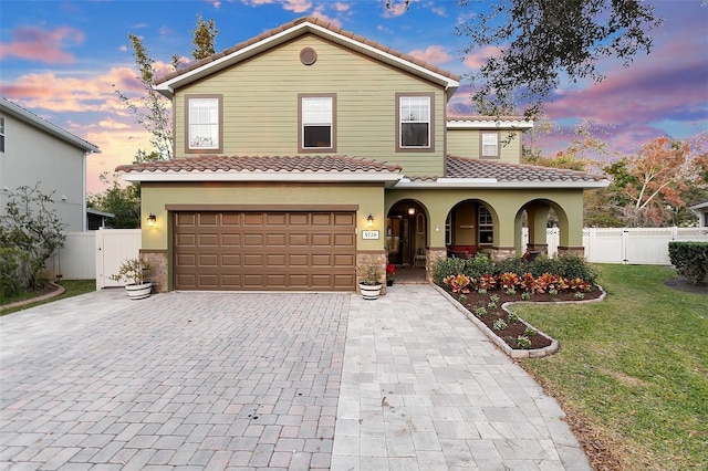 mediterranean / spanish-style house with a tiled roof, decorative driveway, fence, and a gate