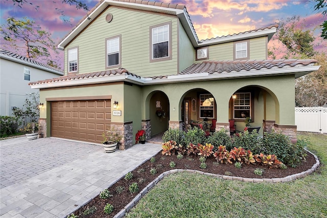 mediterranean / spanish-style house with fence, a porch, stone siding, a tiled roof, and decorative driveway