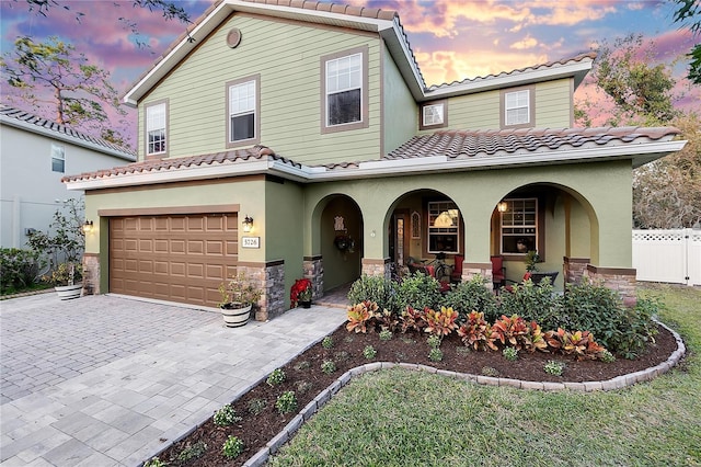 mediterranean / spanish home with a porch, a tile roof, a garage, fence, and stone siding