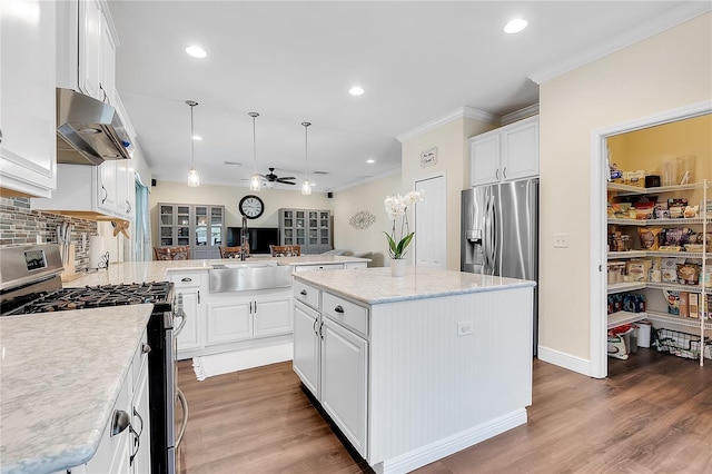 kitchen featuring stainless steel appliances, under cabinet range hood, a ceiling fan, crown molding, and wood finished floors