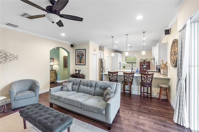 living area featuring crown molding, arched walkways, ceiling fan, dark wood-type flooring, and baseboards