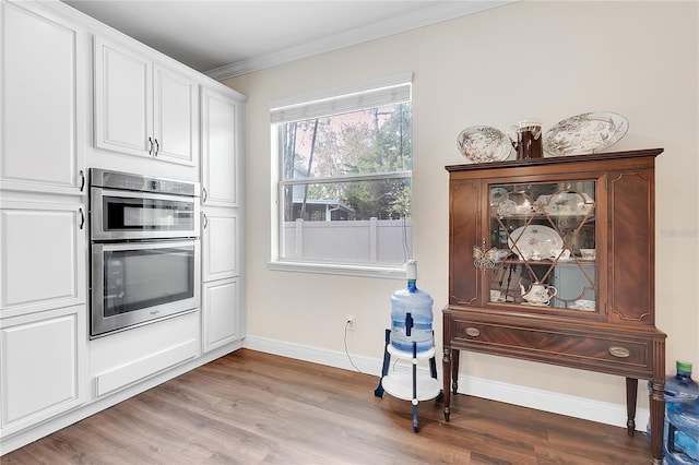 kitchen featuring crown molding, wood finished floors, white cabinets, baseboards, and stainless steel double oven