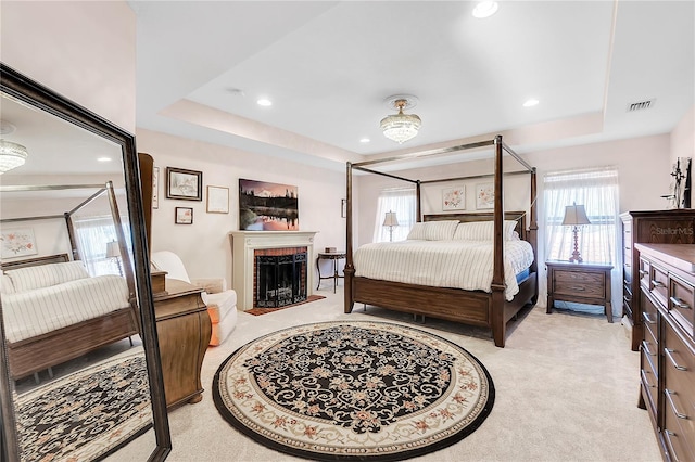 bedroom with a tray ceiling, light carpet, recessed lighting, and a brick fireplace