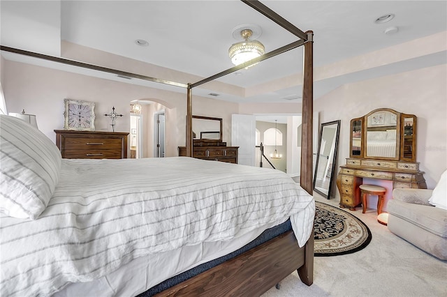carpeted bedroom with arched walkways and a tray ceiling