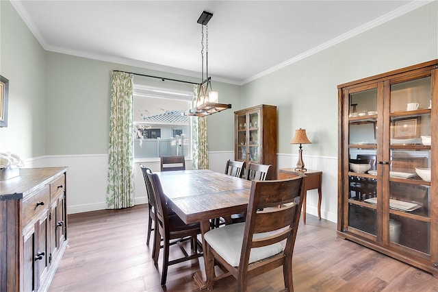 dining space featuring wood finished floors, wainscoting, crown molding, and a chandelier